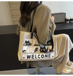 Detail of beige canvas tote bag with cartoon cat pattern and black straps on a shoulder
