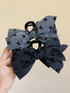 Dettaglio macro della maxi clip per capelli con fiocco in tessuto grigio ricamato