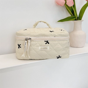 Quilted beige cosmetic bag with black embroidery bows and convenient top handle