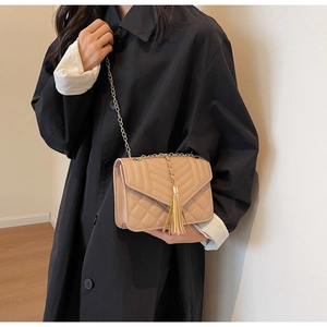 Detail of beige quilted crossbody bag with golden chain strap and fringe tassel charm