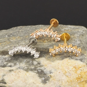 Zircon curved labret studs in silver, gold, and rose gold finishes on black stone