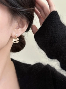 Close-up of golden rocking horse earrings with pearl base and white zircon on model