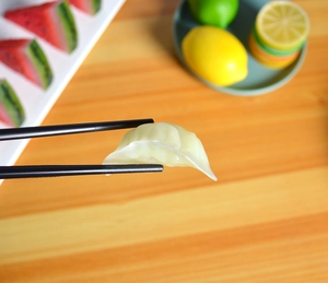 Detailed view of realistic miniature dumplings picked up by black chopsticks in a kitchen set