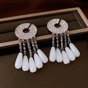 Silver fringe tassel earrings with rhinestones and white teardrop stones on leather background