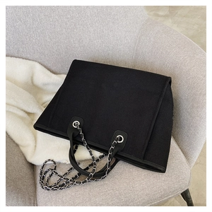 Close-up of black canvas tote bag with metal chain strap on a soft grey sofa