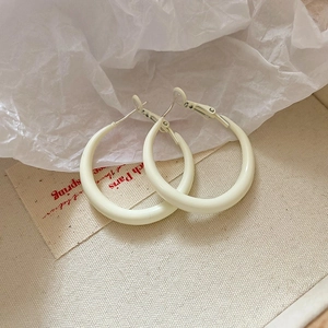 Macro shot of cream white enamel crescent hoop earrings on beige textured canvas