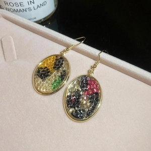 Detailed close-up of golden oval earrings featuring colorful mosaic gemstone inlay