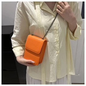 Detail of a bright orange mini crossbody phone bag with fine texture and black chain strap