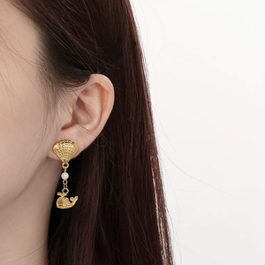 Detailed view of fan-shaped golden earrings with pearl and whale pendant on a model