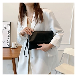 Dettaglio della borsa pochette nera minimalista con elegante cinturino e patta di chiusura