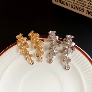 Detailed close-up of gold and silver flower leaf earrings with droplet charms on a white plate