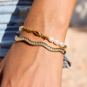 Close-up of a gold-plated rhinestone bangle and white pearl bracelet on a wrist
