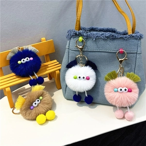 Cute plush monster keychains in multiple colors displayed on a bag and mini bench