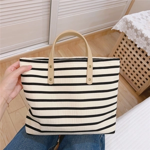 Detail of the black striped canvas bag with leather handle and golden rivet accents