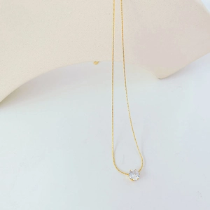 Detailed view of a gold chain necklace with a single round zircon pendant on white stand