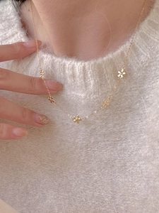 Detail of a dainty gold necklace with five small flowers worn over a white fuzzy sweater