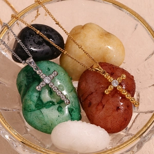 Detail of 18K gold plated cross pendant necklace with zircon stone on glass bowl