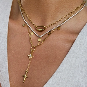 Détail de colliers superposés dorés avec pendentifs étoile et croix sur le cou