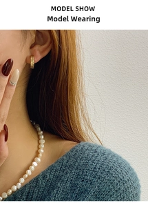 Detail of model wearing gold lava texture hoop earrings with white pearl necklace