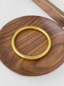 Close-up of golden stainless steel bangle with hammered texture on a wooden tray