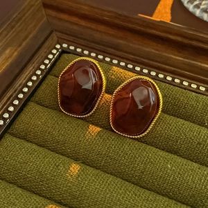 Detailed view of red resin earrings with gold metal edges on green velvet display