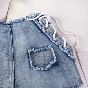 Dettaglio di pantaloncini di jeans blu con lacci laterali e tasca con bordo a frange
