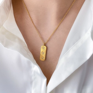 Gold rectangle necklace with three star engravings and cubic zirconia on a white shirt