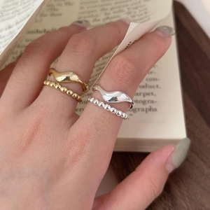 Detail showing stacked gold and silver wave rings on a finger with aesthetic background