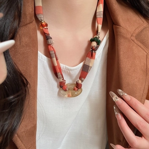 Detail of red-brown checkered fabric knot and amber resin ring pendant on sweater chain