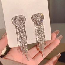 Detail view of heart-shaped rhinestone drop earrings with long shimmering tassels