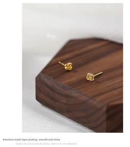 Detail of gold rose stud earrings with refined multi-layer plating on a wooden stand