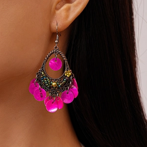 Close-up of bohemian hollow metal drop earrings with pink shell discs on a model