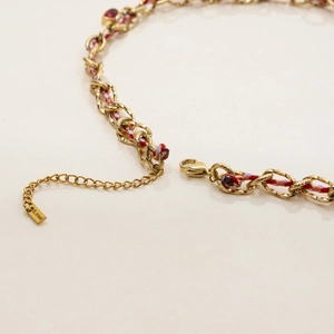 Detail of gold braided necklace with colorful cords, lobster clasp and S.STEEL tag