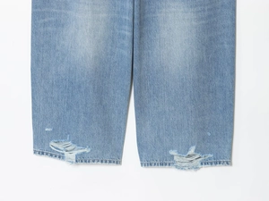 Dettaglio dei fori strappati e dell'orlo sfrangiato sui jeans in denim blu chiaro