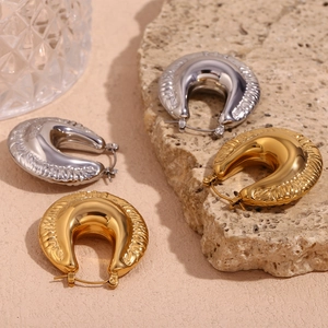 Detail of chunky 18K gold and silver U-shaped hoop earrings with textured radial patterns