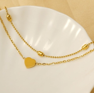 Detail of double-layer gold heart anklet on a white shell-shaped ceramic plate