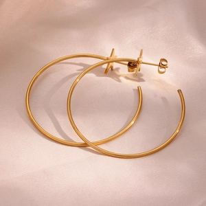 Detailed view of large golden hoop earrings with star studs on a pink silk fabric background