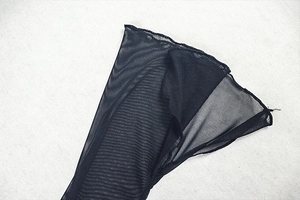Détail du tissu en maille noire montrant la texture fine et l'ourlet d'une robe longue