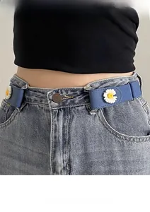 Detailed view of a blue elastic waist belt with white daisy charms on denim jeans