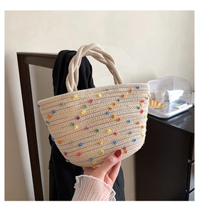 Detail view of woven straw bucket bag featuring colorful pom-pom accents and rope handles