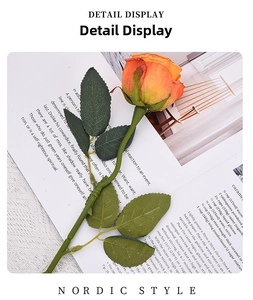 Detail display of a burnt-edge silk rose with orange petals and realistic green leaves