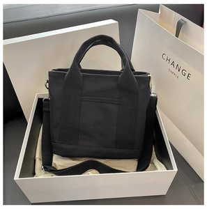 Minimalist black canvas tote bag presented in a white gift box with matching paper bag