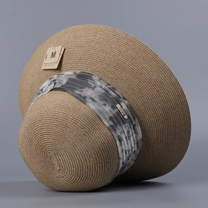 Detail view of woven straw sun hat with marble pattern ribbon and metal logo buckle