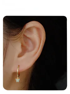 Close-up of gold hoop earring with blue butterfly pendant worn on model ear