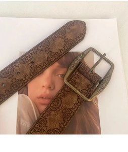 Close-up of vintage brown embossed leather belt with carved metal buckle on a magazine