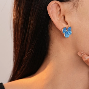 Detail of blue enamel flower stud earrings with gold trim on a model's ear