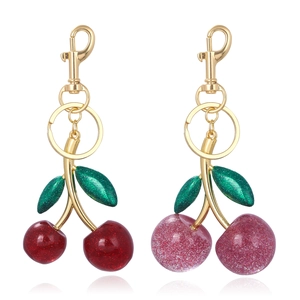 Detail of red and pink cherry keychains with gold lobster clasps and green leaves
