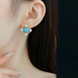 Close-up of vintage gold earring with turquoise stone and pearls worn by a model