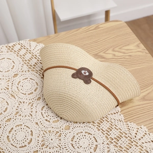 Close-up of beige woven straw sun hat with cute brown bear patch on lace tablecloth