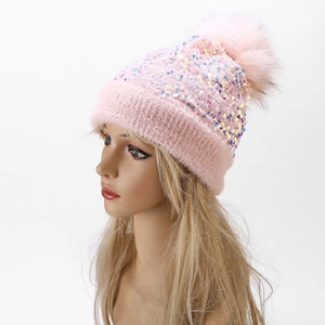 Detailed view of pink knitted beanie with shimmering sequins and fluffy faux fur pom-pom
